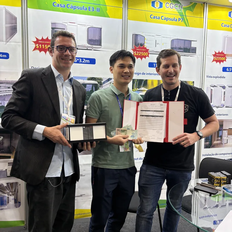 CGCH sales rep with Brazilian buyer holding signed receipt folder, Brazilian Real cash, and sample case at the Casa Cápsula booth