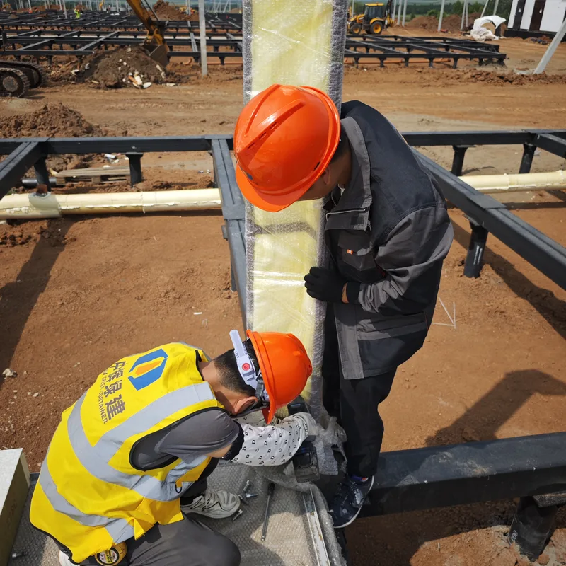 Two CGCH construction workers in CGCH-branded yellow vests installing a structural column at a Russia worksite, LiuGong excavator behind